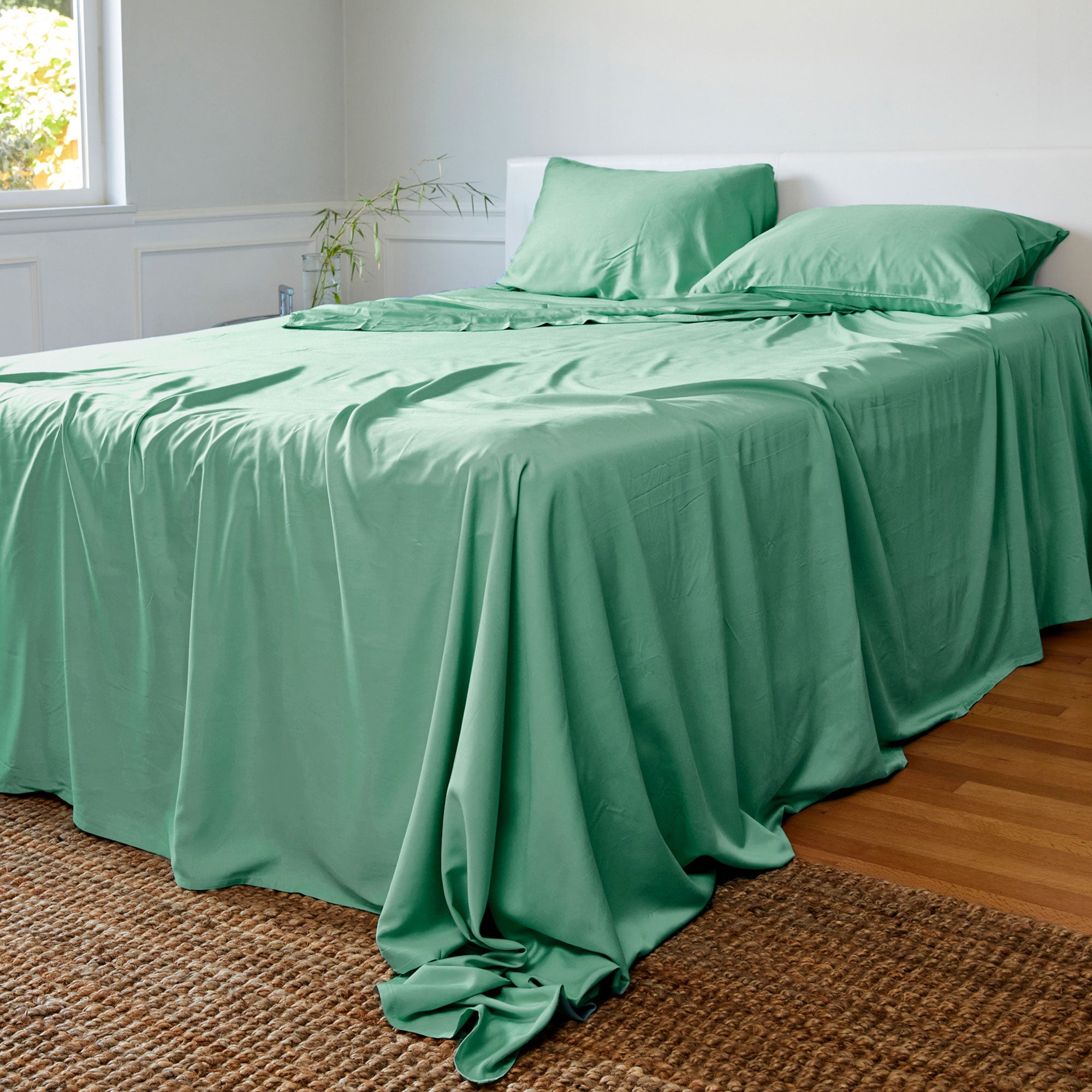 Green bamboo sheets and pillows on a bed in a room with a window and plant.